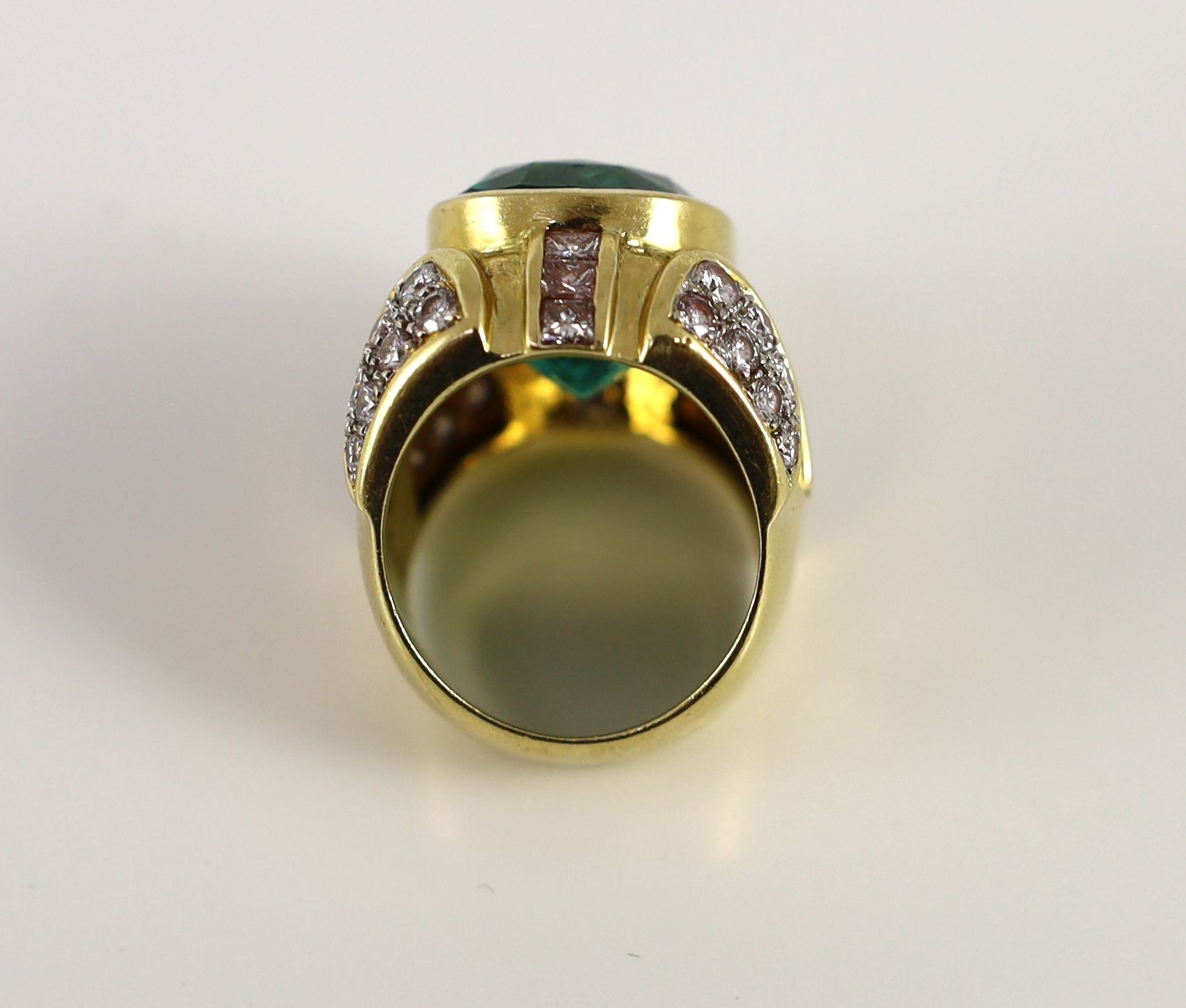 A large gold and single stone oval cut emerald set dress ring, with round and princess cut diamond cluster set shoulders